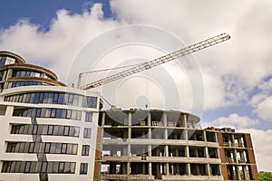 Apartment or office tall building under construction. Brick walls, glass windows, scaffolding and concrete support pillars. Tower