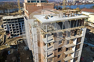 Apartment or office tall building under construction, top view. Brick walls, scaffolding and concrete support pillars. Tower crane