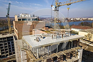 Apartment or office tall building under construction, top view. Brick walls, scaffolding and concrete support pillars. Tower crane