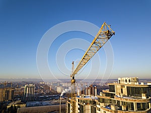 Apartment or office tall building under construction, top view. Tower crane on bright blue sky copy space background, city