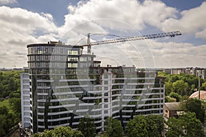 Apartment or office tall building unfinished under construction among green tree tops. Tower cranes on bright blue sky copy space