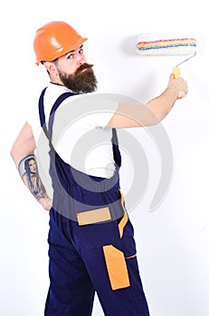 Apartment redecoration. Turn back painter with paint roller in front of white wall. Isolated bearded man with tattoo on