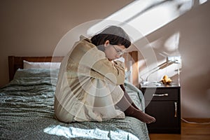 Apathetical teen girl sitting on bed embracing knees feeling procrastination, depression, loneliness