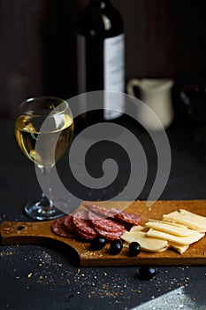 Aperitif table Meat snack, fried sausages, cheese, salami, olives and a glass of wine on a dark table