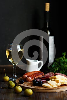 Aperitif table Meat snack, fried sausages, cheese, salami, olives and a glass of wine on a dark table