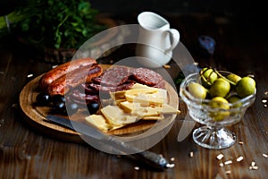 Aperitif table Meat snack, fried sausages, cheese, salami, olives and a glass of wine on a dark table