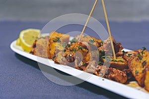 Aperitif or typical Spanish tapa, baby squid or chipirones with garlic and potatoes, served on an elongated white tray with