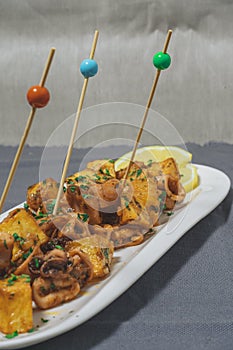 Aperitif or typical Spanish tapa, baby squid or chipirones with garlic and potatoes, served on an elongated white tray with