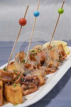 Aperitif or typical Spanish tapa, baby squid or chipirones with garlic and potatoes, served on an elongated white tray with