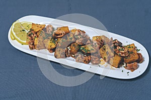Aperitif or typical Spanish tapa, baby squid with garlic and potatoes, served on an elongated white tray with lemon and fork on