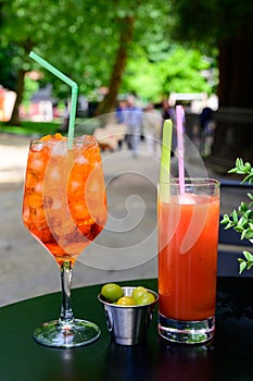 Aperol Sprits summer cocktail with Aperol, prosecco, ice cubes and orange in wine glass and glass of fresh made tomato juice ready