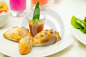 Apetizer of small tomato soup in shotglass and delicious mini empanadas spread around on white plate