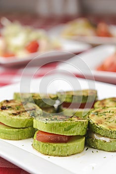 Apetizer from tomatoes, zucchini and mozzarella cheese served on a white plate with other dished on the table