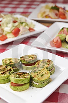 Apetizer from tomatoes, zucchini and mozzarella cheese served on a white plate with other dished on the table