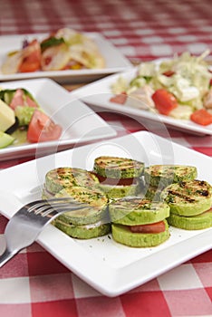 Apetizer from tomatoes, zucchini and mozzarella cheese served on a white plate with other dished on the table