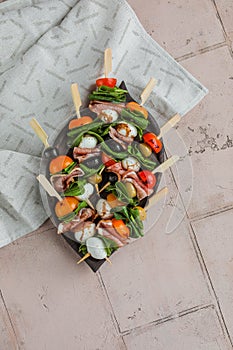 Apetizers on wooden skewers. Snacks from mozzarella, cherry tomatoes, salmon, spinach and olives.