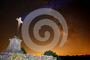 Apocalyptic image of a cross with an orange sky, the Milky Way behind