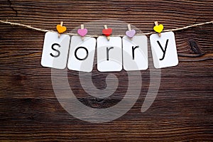 Apologise concept. Cute heart icons garland with text sorry on dark wooden background top view copy space