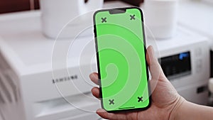 App on mobile phone controls washing machine in smart home. Close up of woman using smartphone with green screen while