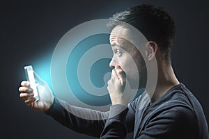 Appalled man looking at his glowing smartphone screen