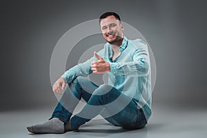 Appealing casual young man sitting on the floor, looking to the camera smiling