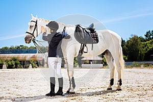 Appealing dark-haired woman standing near white saddle horse