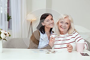 Appealing elder woman and caregiver compiling puzzle