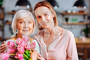 Appealing lady cuddling aged mom with bunch of tulips