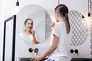 Appealing woman brushing teeth in front of circular mirror