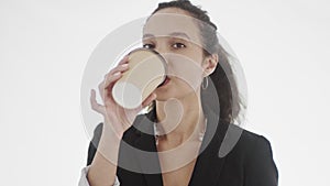 Appealing yound black-haired businesswoman with hoop earrings looks seductively straight at camera and makes a sip from
