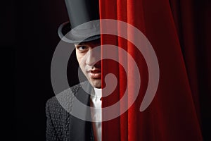 Appearing handsome man magician peeking out from behind stage drapery curtain