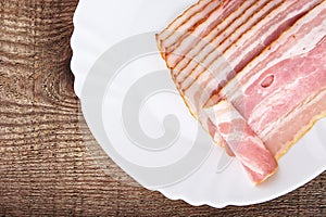 Appetiser from slices of bacon on plate on wooden plank