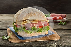Appetising ciabatta sandvich with ham, cheese, tomato and green salad on the wooden background