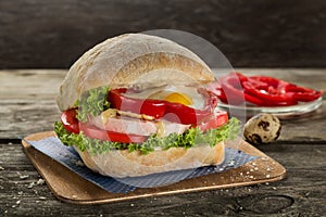Appetising ciabatta sandvich with ham, egg , tomato, sweet red pepper and green salad on the wooden background