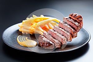 Appetising steak slices levitate above the black plate. Creative shot of steak and french fries on a dark background