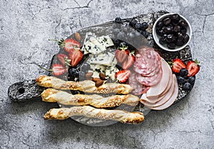 Appetizer board. Gorgonzola, ham, salami, olives, fruit, grassini on a rustic chopping board on a gray background, top view