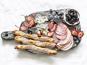 Appetizer board. Gorgonzola, ham, salami, olives, fruit, grassini sticks on a rustic chopping board on a light background, top