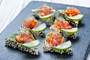 Appetizer canape with chopped vegetables and sesame on stone slate background close up.