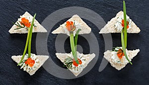 Appetizer canape with red caviar and cream cheese on stone slate background close up.