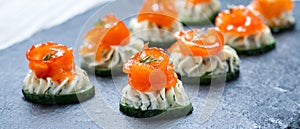 Appetizer canape with salmon, cucumber and cream cheese on stone slate background close up.