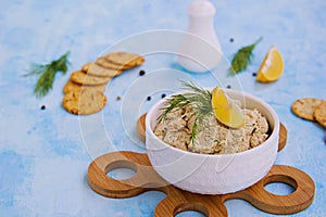 Appetizer, fish pate from mackerel, boiled eggs and onions in a white ceramic bowl on a blue concrete background