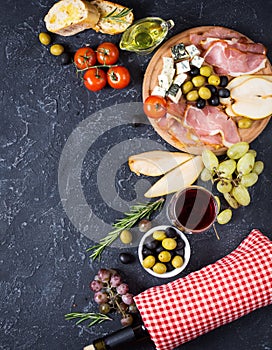 Appetizer, italian antipasto, ham, olives, cheese, bread, grapes, pear and wine on dark stone background. Top view