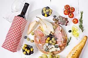 Appetizer, italian antipasto, ham, olives, cheese, bread, grapes, pear and wine on white wood background