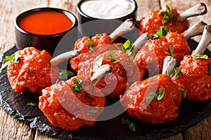 Appetizer Lollipops deep-fried red chicken wings served with sauces close-up on a slate board. horizontal