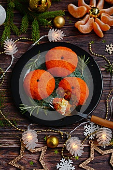 An appetizer for the New Year`s table made in the form of tangerines on a dark plate against a background of decorations and