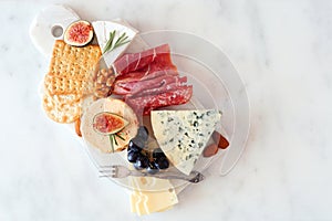 Appetizer platter with assorted cheeses and meats, top view on white marble