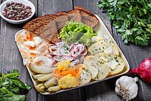 Appetizer platter, baked potato, delicious sliced pork fat with spices, sliced smoked fish with onions, pickles and bread on woode