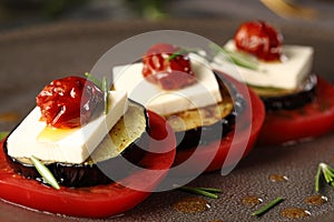 Appetizer of ripe tomatoes, feta cheese, fried eggplant, sun dried tomatoes in oil and rosemary leaves