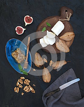 Appetizer set. Roasted pears, goat cheese on rustic dark wooden board, fig, honey and walnuts over black stone