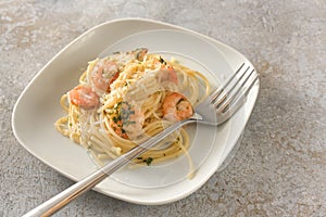 Appetizer spaghetti with shrimps, garlic and herbs, Mediterranean seafood on a small plate, rustic gray background with copy space